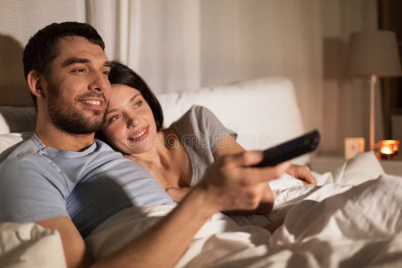 Coppie felici che guardano TV a letto alla notte a casa immagine stock Coppie felici che guardano TV a letto alla notte a casa immagine stock
