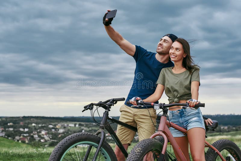 Coppie felici con i fatbikes che prendono selfie dallo smartphone all'aperto immagine stock Coppie felici con i fatbikes che prendono selfie dallo smartphone all'aperto immagine stock