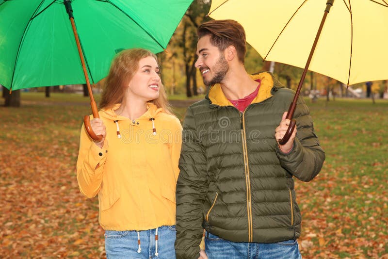 Coppie felici con la camminata degli ombrelli fotografia stock libera da diritti Coppie felici con la camminata degli ombrelli fotografia stock libera da diritti