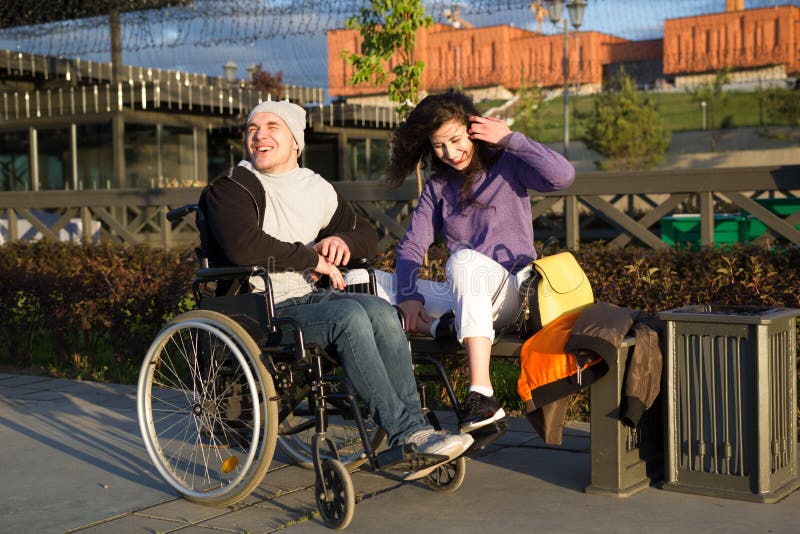 Coppie felici - uomo disabile in sedia a rotelle che parla con la giovane donna attraente che enjoing il tramonto fotografia stock Coppie felici - uomo disabile in sedia a rotelle che parla con la giovane donna attraente che enjoing il tramonto fotografia stock
