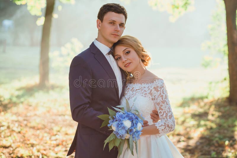 Coppie giovani attraenti di stupore nel giorno delle nozze sposa in vestito lungo bianco elegante ed in mazzo blu a disposizione, fotografie stock libere da diritti Coppie giovani attraenti di stupore nel giorno delle nozze sposa in vestito lungo bianco elegante ed in mazzo blu a disposizione, fotografie stock libere da diritti