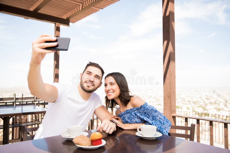 Coppie latine che prendono selfie mentre sedendosi in caffè all'aperto fotografie stock Coppie latine che prendono selfie mentre sedendosi in caffè all'aperto fotografie stock