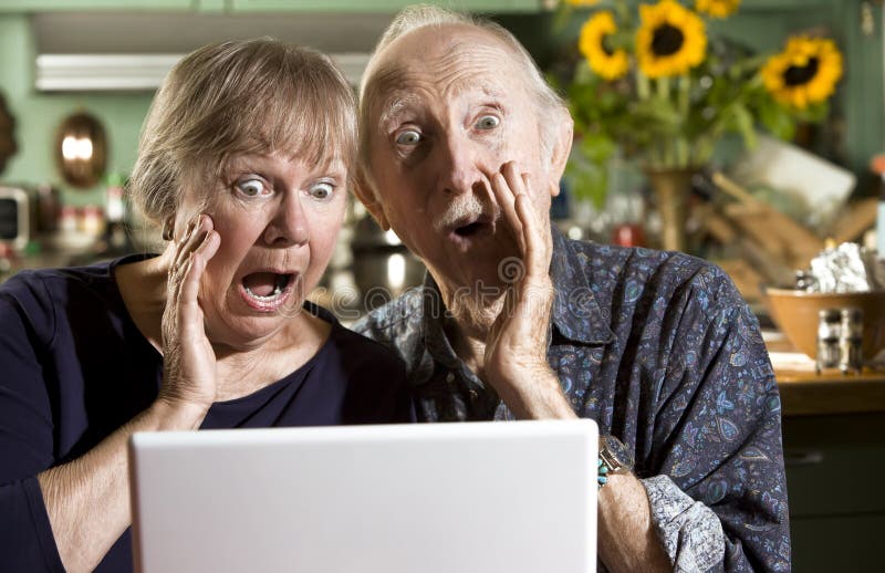 Shocked Senior Couple in their Dining Room with a Laptop Computer. Shocked Senior Couple in their Dining Room with a Laptop Computer