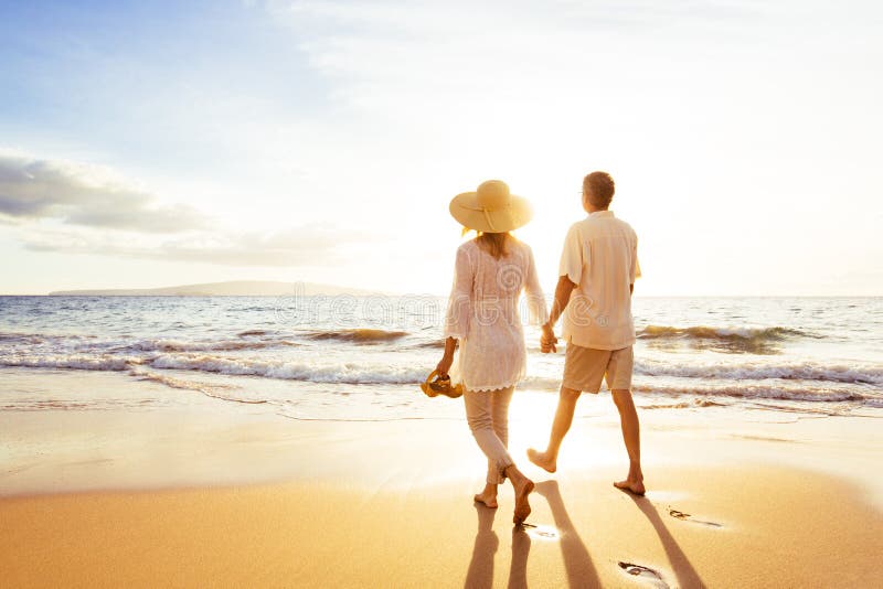 Coppie mature che camminano sulla spiaggia al tramonto fotografia stock