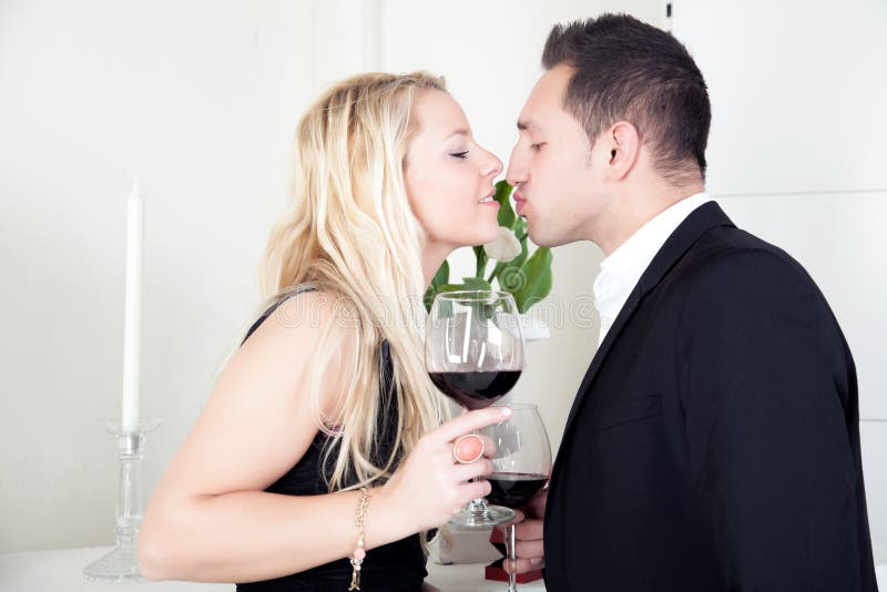 Attractive elegant young couple in love kissing while holding large glasses of red wine in their hands as they celebrate their love and a special occasion. Attractive elegant young couple in love kissing while holding large glasses of red wine in their hands as they celebrate their love and a special occasion