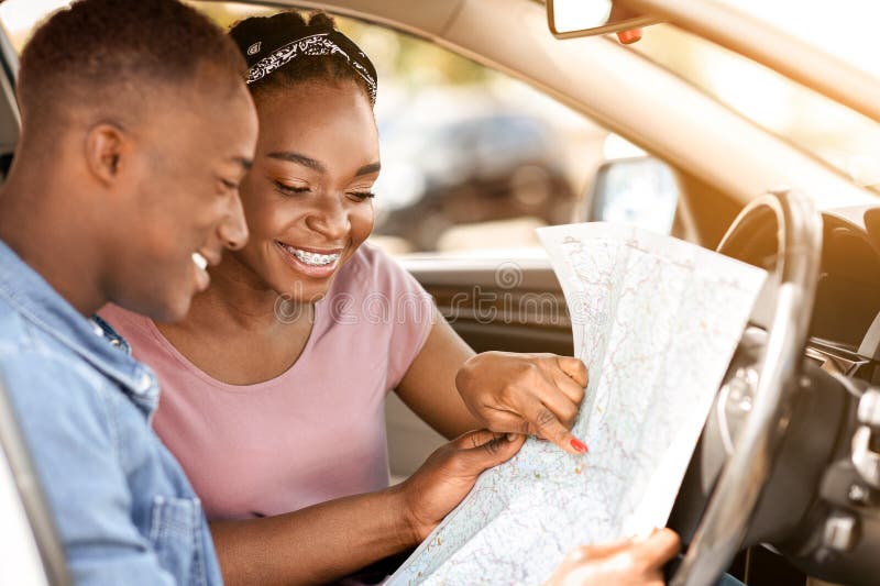 Coppie nere entusiaste leggono una mappa mentre fanno un viaggio in macchina fotografia stock