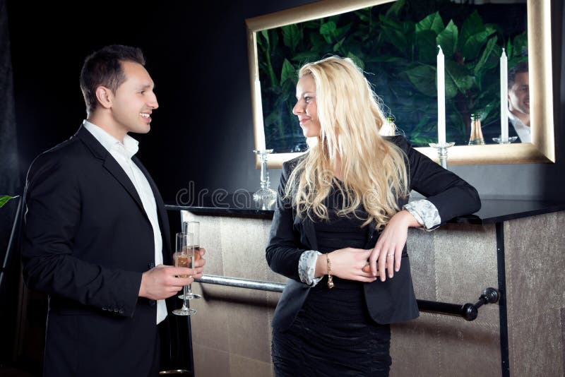 Romantic beautiful young couple in love staring into each others eyes as they stand in front of a fireplace with flutes of champagne on an elegant evening out. Romantic beautiful young couple in love staring into each others eyes as they stand in front of a fireplace with flutes of champagne on an elegant evening out.