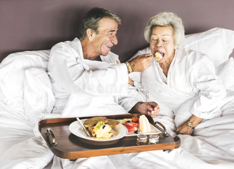 Coppie senior che mangiano prima colazione a letto fotografia stock Coppie senior che mangiano prima colazione a letto fotografia stock