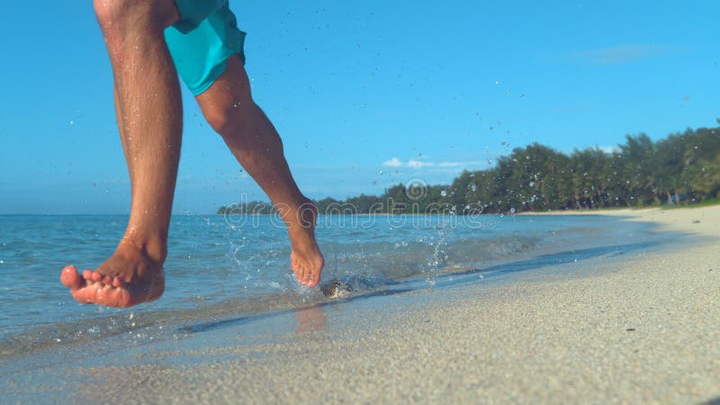 COPY SPACE: Unrecognizable man jogs barefoot down sandy beach and past camera. stock photos