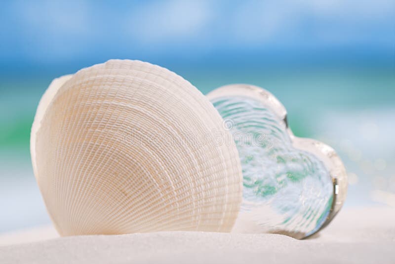 White sea shell with heart glass on beach and sea blue background. White sea shell with heart glass on beach and sea blue background