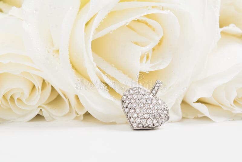 Corazón del colgante de oro de la joyería con los diamantes en fondo del ramo de las rosas blancas con el espacio de la copia Maq fotos de archivo Corazón del colgante de oro de la joyería con los diamantes en fondo del ramo de las rosas blancas con el espacio de la copia Maq fotos de archivo
