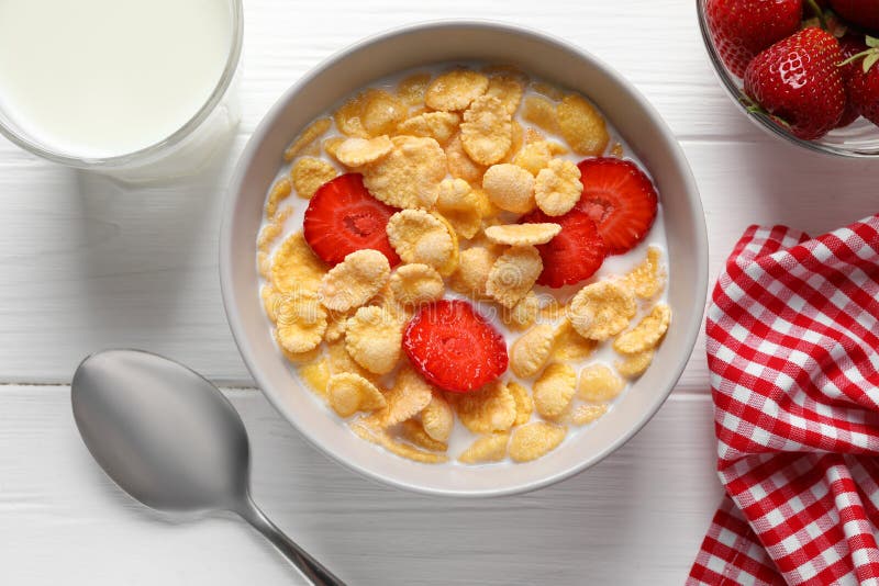 Corn flakes with strawberries in bowl served on wooden table, flat lay