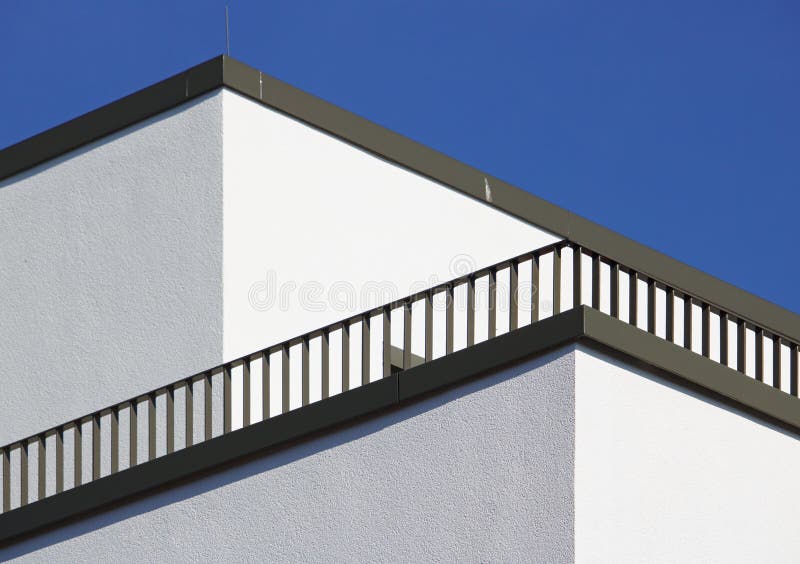 Corner of a white building with diagonal balcony railing and blue sky