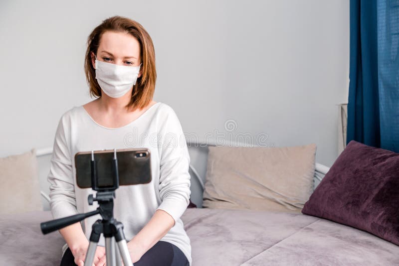 Coronavirus Mujer en cuarentena por disfrazar con máscara protectora, trabaja desde casa y usa teléfono móvil en el sofá Pandemia imagen de archivo libre de regalías Coronavirus Mujer en cuarentena por disfrazar con máscara protectora, trabaja desde casa y usa teléfono móvil en el sofá Pandemia imagen de archivo libre de regalías