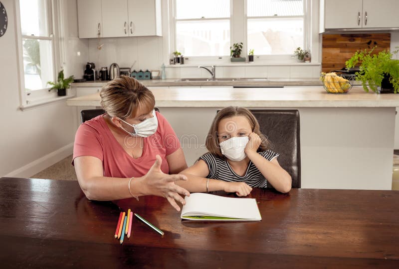 Coronavirus school closures and lockdown. Mum and bored daughter with masks studying online at home stock photo Coronavirus school closures and lockdown. Mum and bored daughter with masks studying online at home stock photo