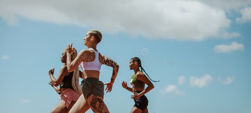 Athletes running on racetrack outdoors. Young females competing in a track event. Athletes running on racetrack outdoors. Young females competing in a track event