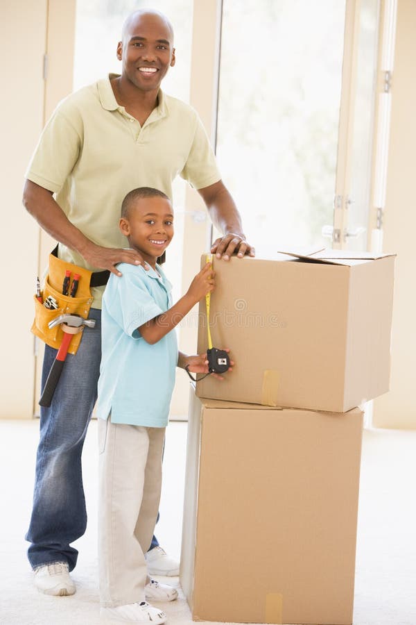 Father wearing tool belt standing by son and boxes in new home smiling. Father wearing tool belt standing by son and boxes in new home smiling