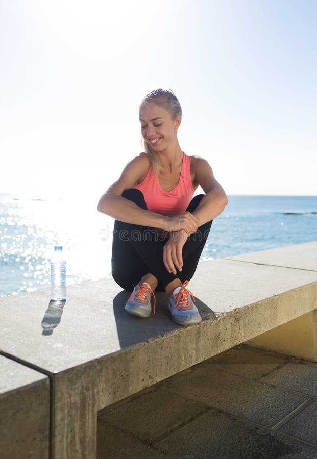 Corridore femminile felice che si rilassa dopo l'addestramento di forma fisica nell'aria fresca nel giorno soleggiato fotografie stock Corridore femminile felice che si rilassa dopo l'addestramento di forma fisica nell'aria fresca nel giorno soleggiato fotografie stock