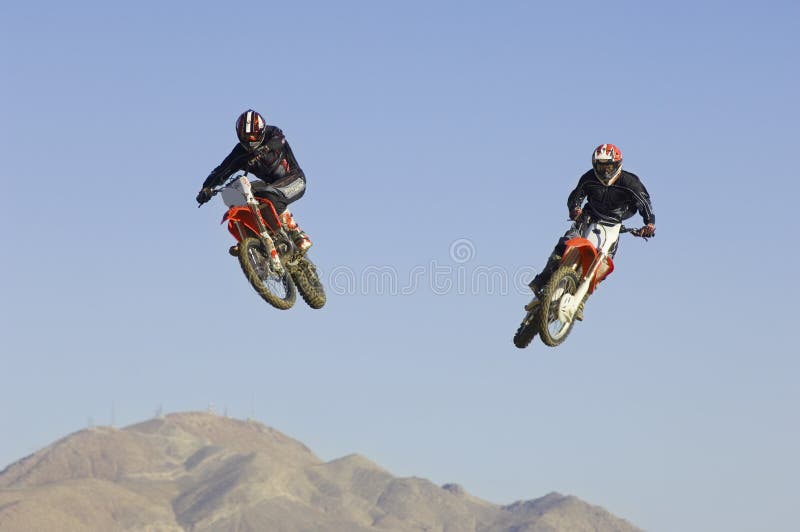Corridori di motocross che eseguono acrobazia nell'a mezz'aria contro il cielo blu