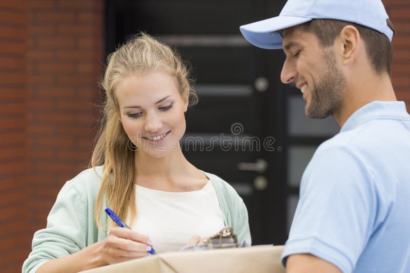 Corriere e ricevuta di firma sorridente della donna sulla scatola immagine stock Corriere e ricevuta di firma sorridente della donna sulla scatola immagine stock