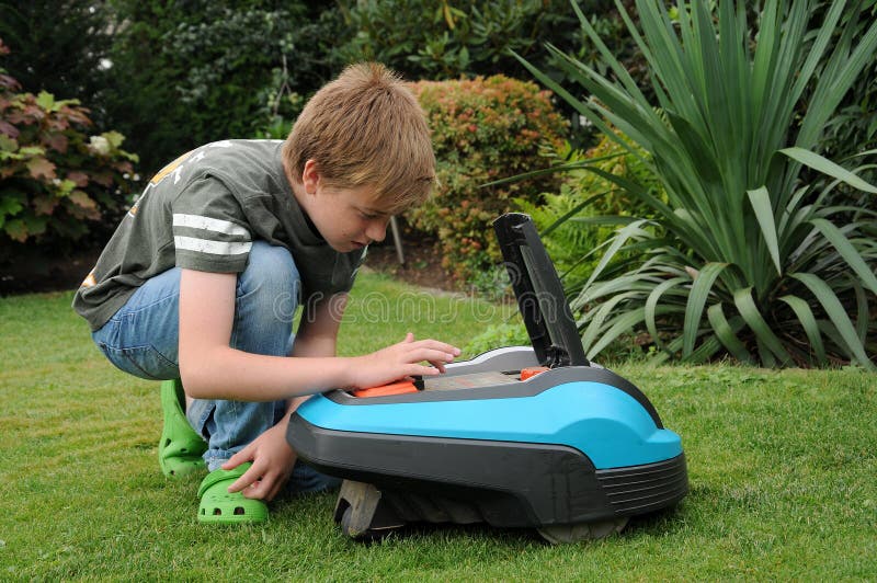 Teenager boy keys in the code number and started robotic lawn mover. Teenager boy keys in the code number and started robotic lawn mover