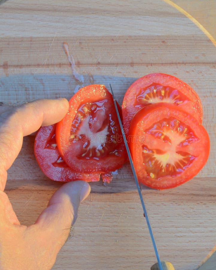 Cortar un tomate con las manos con un cuchillo en una tabla de cortar de madera en la puesta del sol fotos de archivo libres de regalías