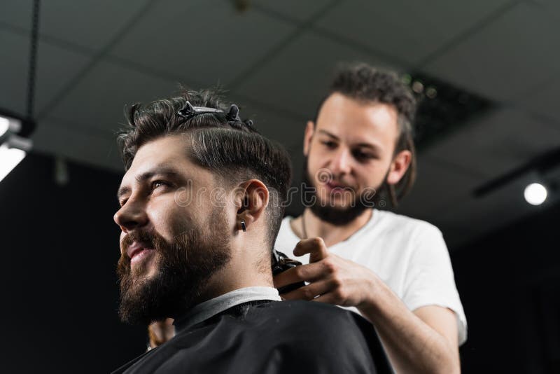 Corte de cabelo de máquina fraca para um homem barbudo bonito na barbearia. corte de cabelo com transição suave.