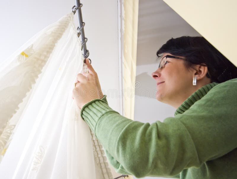 A woman hanging new net curtains at a window. A woman hanging new net curtains at a window.