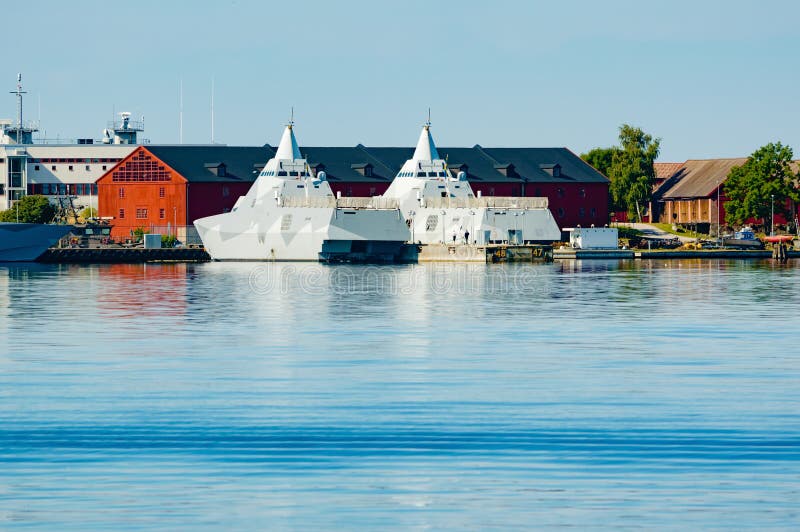 Karlskrona, Sweden - August 03, 2015: Two Visby class Swedish navy stealth corvettes moored at the naval base harbor as seen from the water looking in. Karlskrona, Sweden - August 03, 2015: Two Visby class Swedish navy stealth corvettes moored at the naval base harbor as seen from the water looking in.