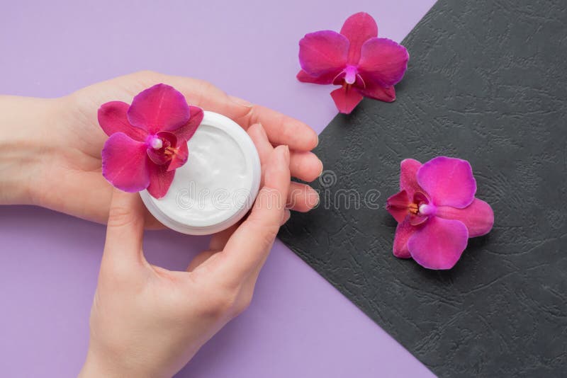 Cosmetic background with hands, soft white cream and fragile magenta colored orchids.Moisturizing facial cream.