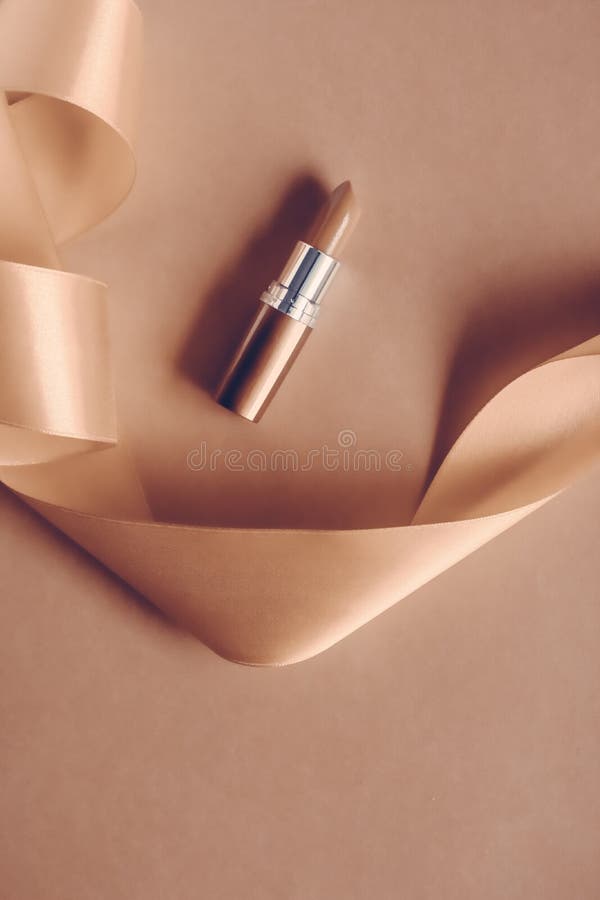 Luxury lipstick and silk ribbon on beige holiday background, make-up and cosmetics flatlay for beauty brand product design royalty free stock photography Luxury lipstick and silk ribbon on beige holiday background, make-up and cosmetics flatlay for beauty brand product design royalty free stock photography