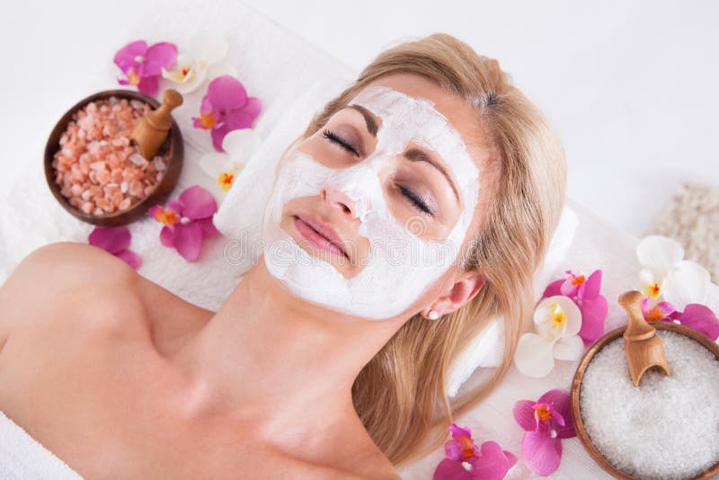 Cosmetician applying facial mask on face of woman. Cosmetician Applying Facial Mask To The Face Of Young Beautiful Woman In Spa Salon stock images