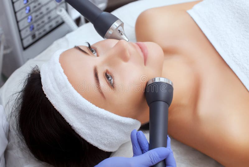 Cosmetologist maakt de procedure het ultrasone schoonmaken van de gezichtshuid van een mooie, jonge vrouw in een schoonheidssalon