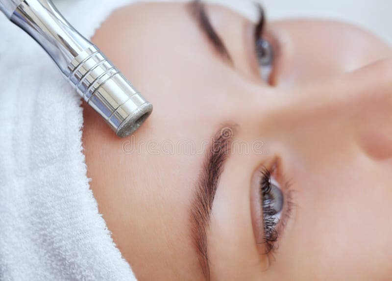 Cosmetologist maakt de procedure Microdermabrasion van de gezichtshuid van een mooie, jonge vrouw in een schoonheidssalon