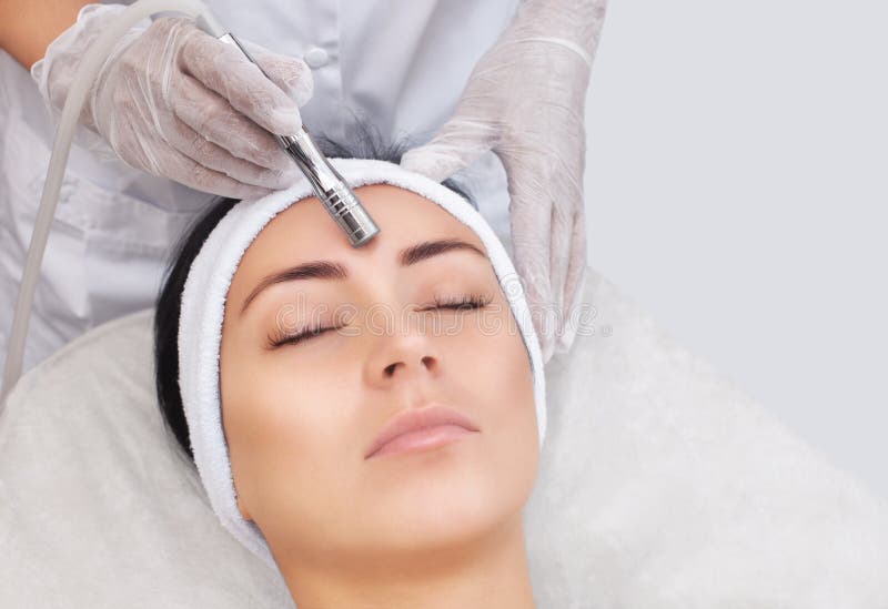 Cosmetologist maakt de procedure Microdermabrasion van de gezichtshuid van een mooie, jonge vrouw