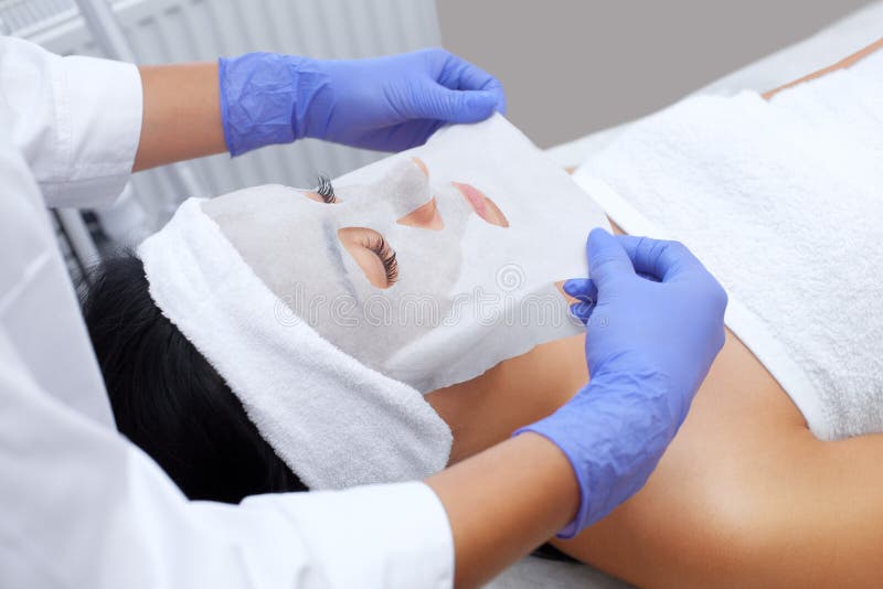 Cosmetologist voor procedure die om de huid te reinigen en te bevochtigen, een bladmasker toepassen op het gezicht van een jonge