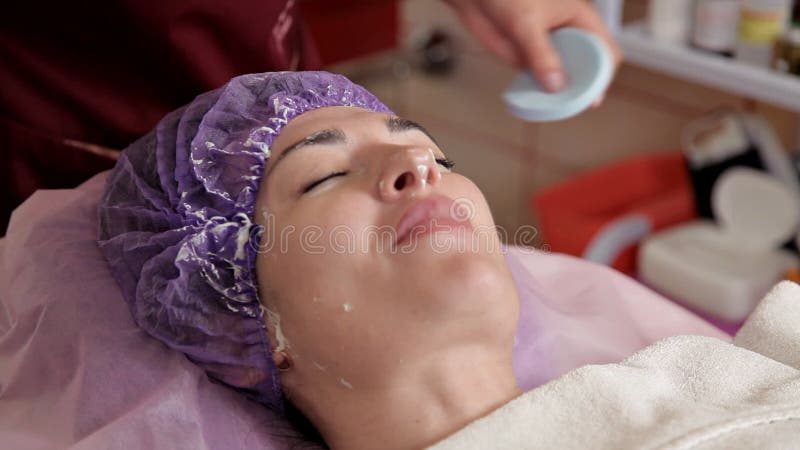 Cosmetologist που αφαιρεί τη μάσκα άλατος αλγινικού οξέος από τη νέα γυναίκα