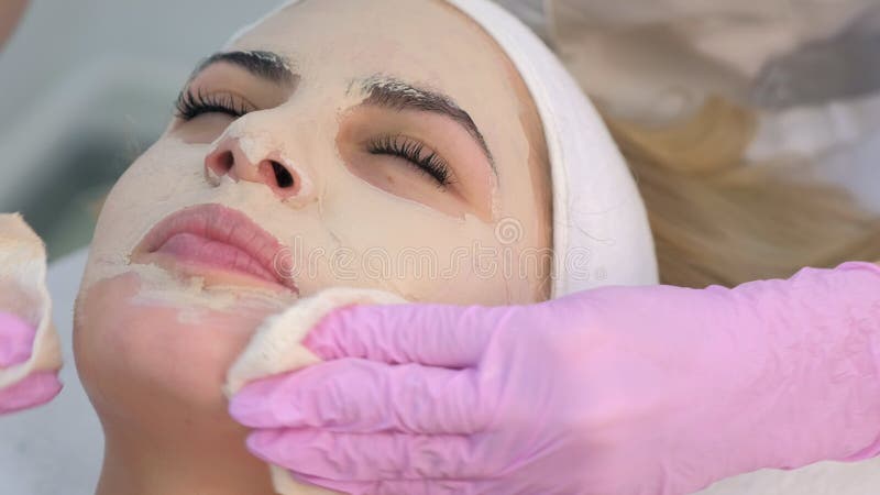 Cosmetologist в перчатках, вытирая маску по уходу за кожей из портрет: лица женщины.