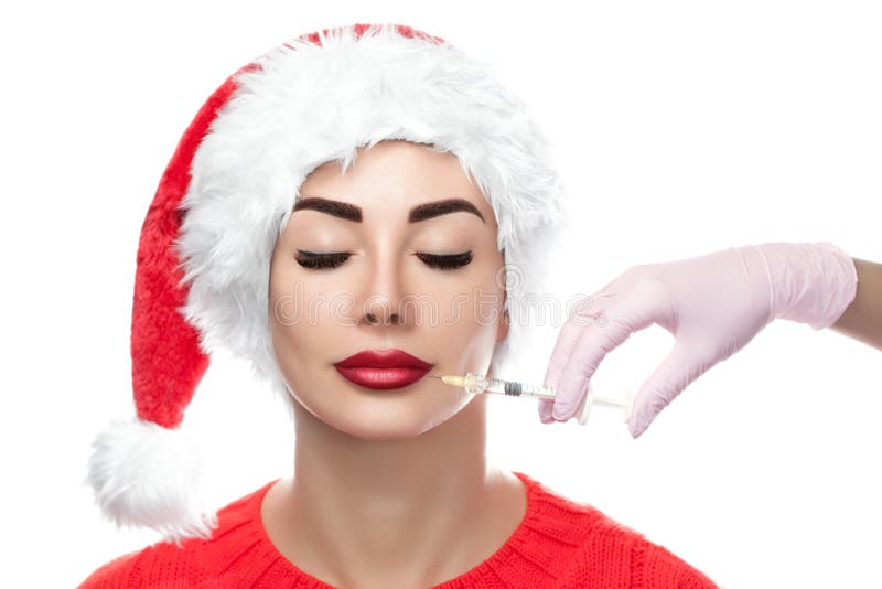 Cosmetologist доктора делает процедуру по впрыски Botox на коже стороны красивой женщины в шляпе Санта Клауса стоковое фото rf Cosmetologist доктора делает процедуру по впрыски Botox на коже стороны красивой женщины в шляпе Санта Клауса стоковое фото rf