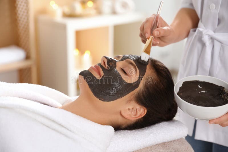 Cosmetologist прикладывая черную маску на сторону женщины стоковые изображения rf Cosmetologist прикладывая черную маску на сторону женщины стоковые изображения rf