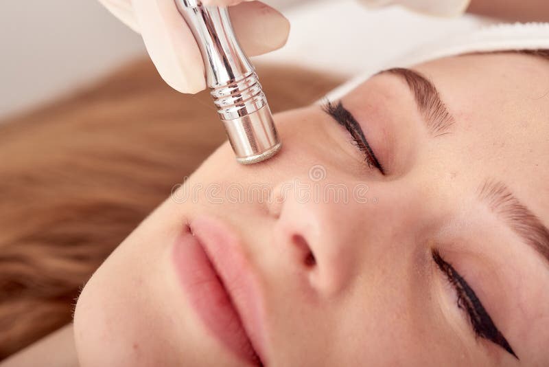 Cosmetologisten gör tillvägagångssättet Microdermabrasion av den ansikts- huden av en härlig ung kvinna i en skönhetsalong fotografering för bildbyråer