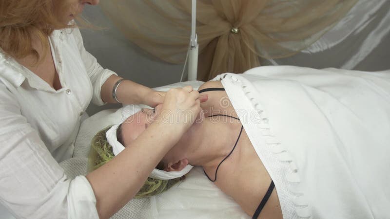 Cosmetologisten torkar ut framsidan, hals vid den våta servetten till den vuxna kvinnan i skönhetsalong lager videofilmer Cosmetologisten torkar ut framsidan, hals vid den våta servetten till den vuxna kvinnan i skönhetsalong lager videofilmer