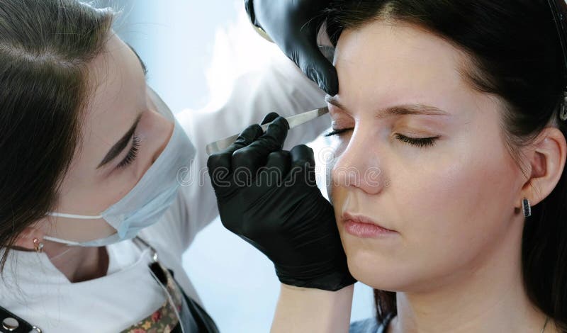 Cosmetologisten utför tillvägagångssättet av korrigeringsögonbrynet med pincett för closeupeyedroppers hög för upplösning sikt my royaltyfri fotografi Cosmetologisten utför tillvägagångssättet av korrigeringsögonbrynet med pincett för closeupeyedroppers hög för upplösning sikt my royaltyfri fotografi