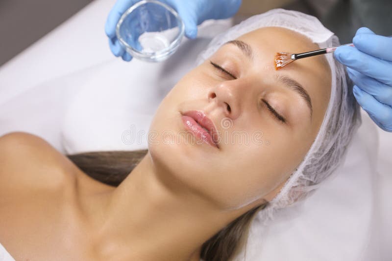 Cosmetologo che applica prodotti chimici di scorza sulla faccia del cliente in salone
