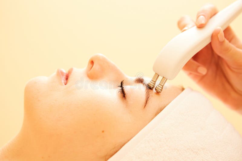 Cosmetology. Beautiful Woman At Spa Clinic Receiving Stimulating Electric Facial Treatment From Therapist. Closeup Of