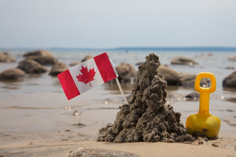 A Toy Spade, Mud Castle and Flag of Canada on a Sea Shore. A Toy Spade, Mud Castle and Flag of Canada on a Sea Shore