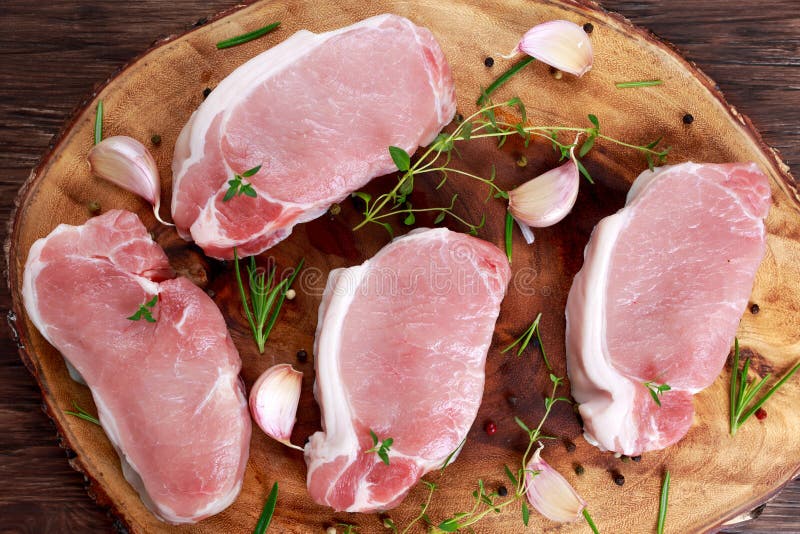 Costeletas de carne de porco sem ossos frescas cruas com ervas Na placa de madeira