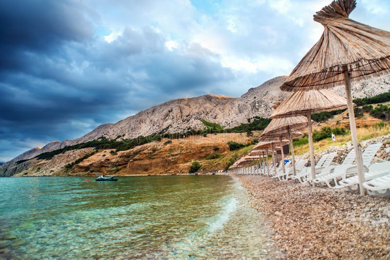 Costline di Rocky Adriatic Sea con gli ombrelli della paglia, i sunbends e chiara acqua Paesaggio del mare, località di soggiorno fotografie stock libere da diritti Costline di Rocky Adriatic Sea con gli ombrelli della paglia, i sunbends e chiara acqua Paesaggio del mare, località di soggiorno fotografie stock libere da diritti