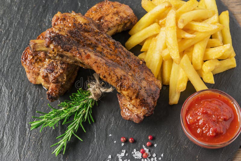 Costole di carne di maiale al forno con le patate fritte e la salsa rossa fotografia stock libera da diritti Costole di carne di maiale al forno con le patate fritte e la salsa rossa fotografia stock libera da diritti