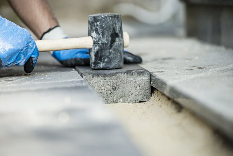 Builder laying a paving stone or brick tamping it down with a rubber mallet. Builder laying a paving stone or brick tamping it down with a rubber mallet.